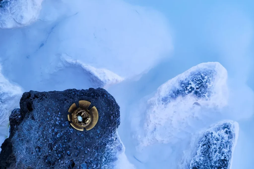 Broche ronde Strokkur en laiton et labradorite posée sur la roche volcanique du Blue Lagoon en Islande, illustrant l'intention en photographie de bijoux